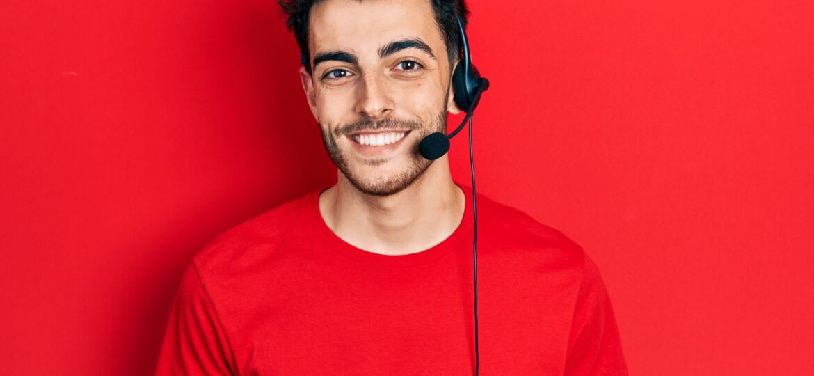 Young hispanic man wearing call center agent headset looking positive and happy standing and smiling with a confident smile showing teeth